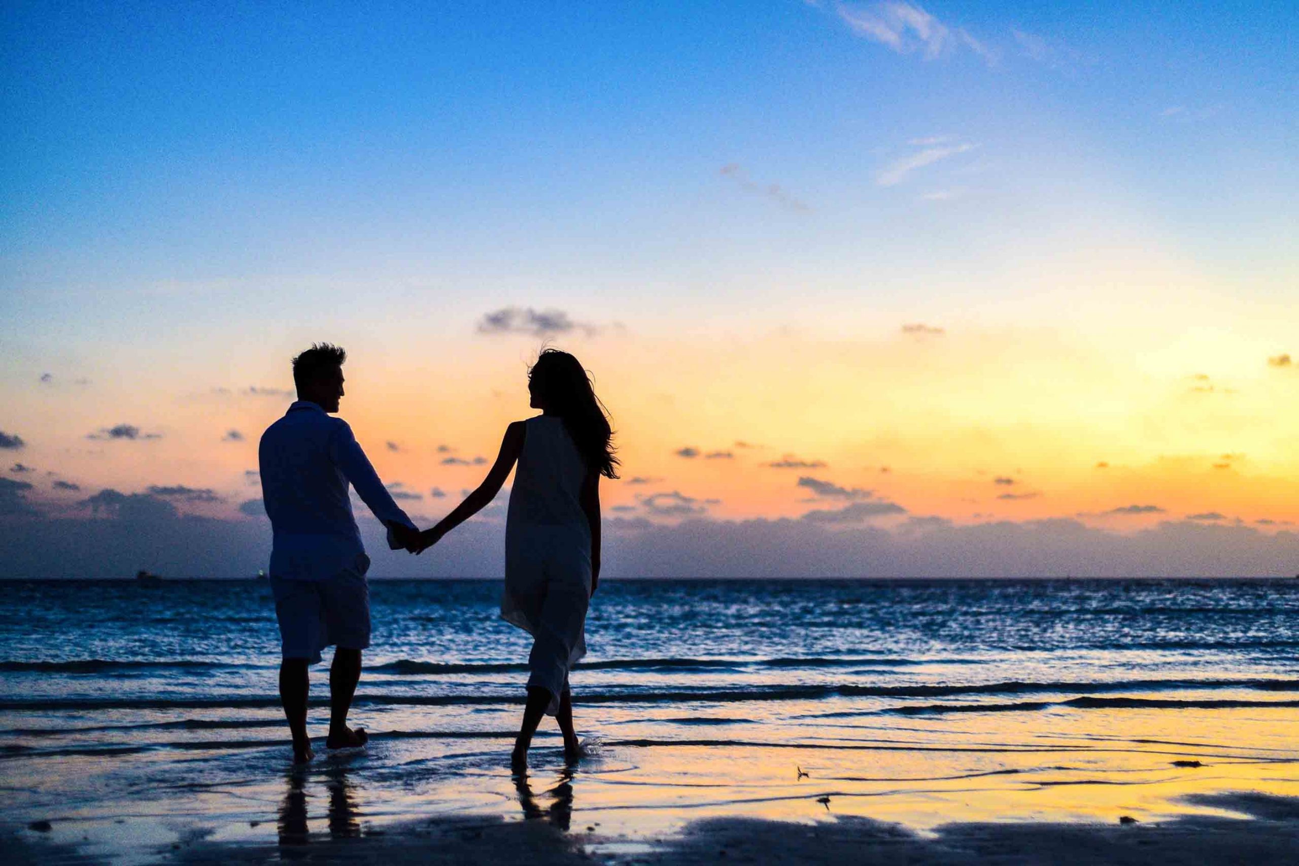 A romantic image of man and woman walking together on the beach and holding hands with sunset in the background